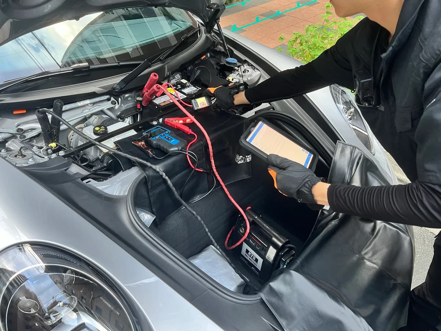 手袋を着けた隊員が、養生した車両でバッテリーと測定機器・タブレットを確認する様子
